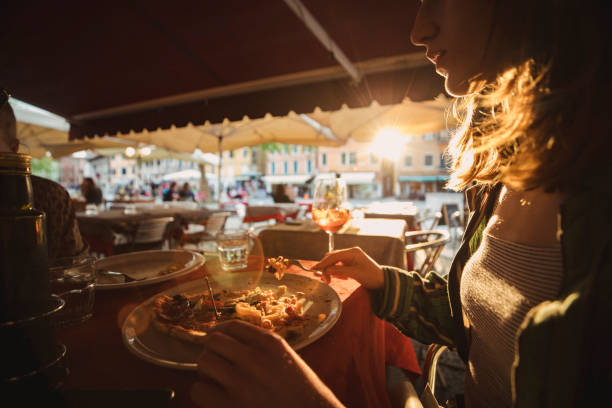 Dining on a Summer Evening A side view shot of a lady eating pizza at an outdoor restaurant under the sunlight. outdoor dining photos stock pictures, royalty-free photos & images