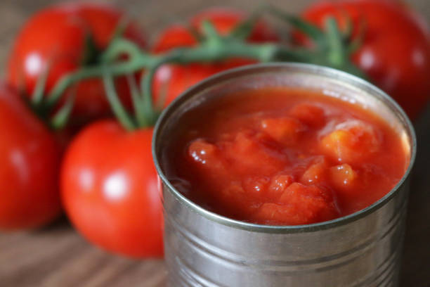 imagen de lata genérica sin marca de trozos de tomatepicado / passata enlatada del supermercado con gran planta de tomate de vid en tabla de cortar madera / tablero de pan, en cubos y picados tomates enlatados italianos puré de puré, pelado para salsa d - peeled juicy food ripe fotografías e imágenes de stock