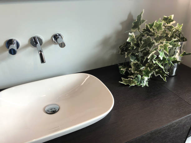 immagine di armadio bagno bagno in legno con lavandino bagno in ceramica bianca e asciugamani piegati, realistica pianta di edera finta artificiale che cresce in vaso d'argento, con foglie variegate di seta di plastica e fogliame, finale comune edera ingle - sink bathroom pedestal tile foto e immagini stock