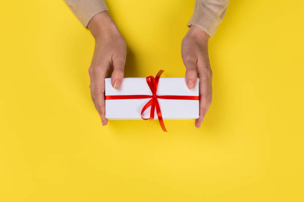 istock Womans hands holding gift or present box on Yellow table top view. Flat lay  for birthday or New Year. 1162944116
