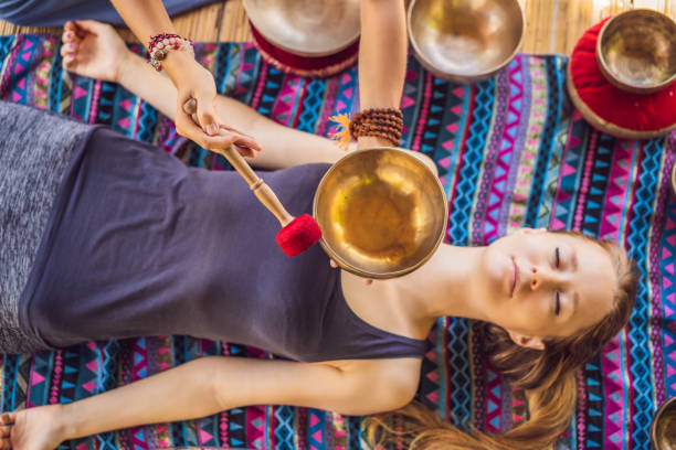 bol de chant de cuivre de bouddha de népal au salon de spa. jeune belle femme faisant la thérapie de massage chantant des cuvettes dans le spa contre une chute d'eau. thérapie sonore, loisirs, méditation, mode de vie sain et concept de soins du corps - tibetan culture music sound recovery photos et images de collection