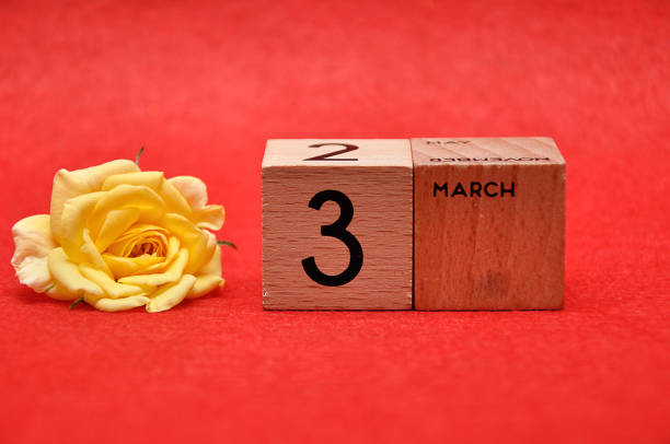 istock 3 March on wooden blocks with a yellow rose on a red background 1162952295