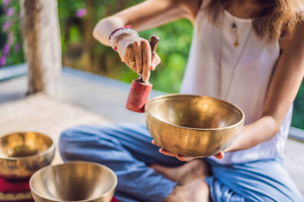 frau spielt auf tibetischen klangschale, während sie auf yogamatte gegen einen wasserfall sitzt. vintage tonnen. schönes mädchen mit mala perlen meditieren - kitchen utensil audio stock-fotos und bilder