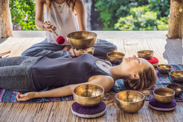 Nepal Buddha copper singing bowl at spa salon. Young beautiful woman doing massage therapy singing bowls in the Spa against a waterfall. Sound therapy, recreation, meditation, healthy lifestyle and body care concept. cuenco de canto de cobre nepal buda en el salón de spa. joven hermosa mujer haciendo terapia de masaje cantando cuencos en el spa contra una cascada. terapia de sonido, recreación, meditación, estilo de vida saludable y concepto de cuidado corporal