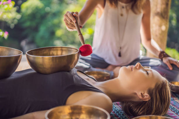 nepal buddha kupfer klangschale im spa-salon. junge schöne frau macht massage-therapie-singschalen im spa gegen einen wasserfall. klangtherapie, erholung, meditation, gesunder lebensstil und körperpflegekonzept - tibetan culture stock-fotos und bilder