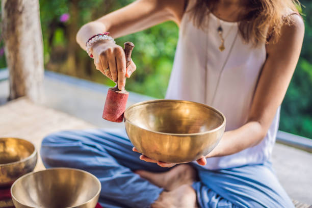 frau spielt auf tibetischen klangschale, während sie auf yogamatte gegen einen wasserfall sitzt. vintage tonnen. schönes mädchen mit mala perlen meditieren - tibetan culture stock-fotos und bilder