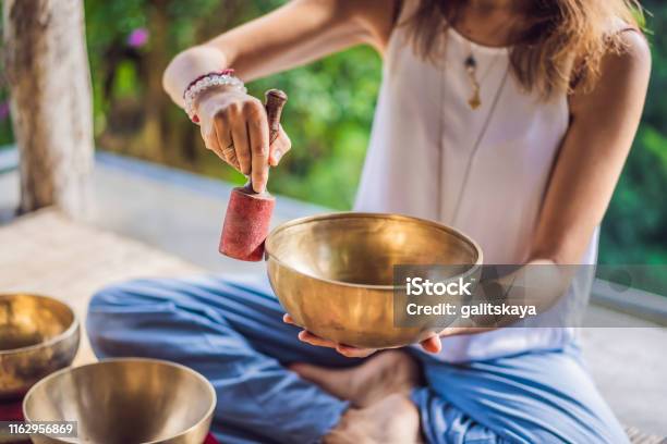Woman Playing On Tibetan Singing Bowl While Sitting On Yoga Mat Against A Waterfall Vintage Tonned Beautiful Girl With Mala Beads Meditating Stock Photo - Download Image Now