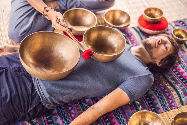 istock Nepal Buddha copper singing bowl at spa salon. Young beautiful man doing massage therapy singing bowls in the Spa against a waterfall. Sound therapy, recreation, meditation, healthy lifestyle and body care concept 1162957657