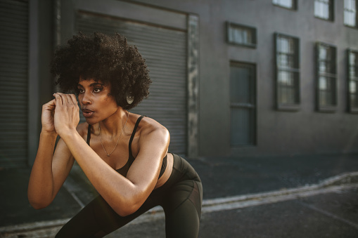 Young woman practicing squats in city. Female athlete exercising outdoors in morning.