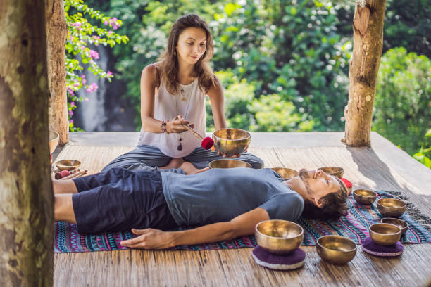 Nepal Buddha copper singing bowl at spa salon. Young beautiful man doing massage therapy singing bowls in the Spa against a waterfall. Sound therapy, recreation, meditation, healthy lifestyle and body care concept