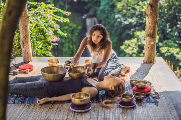 Nepal Buddha copper singing bowl at spa salon. Young beautiful woman doing massage therapy singing bowls in the Spa against a waterfall. Sound therapy, recreation, meditation, healthy lifestyle and body care concept. cuenco de canto de cobre nepal buda en el salón de spa. joven hermosa mujer haciendo terapia de masaje cantando cuencos en el spa contra una cascada. terapia de sonido, recreación, meditación, estilo de vida saludable y concepto de cuidado corporal