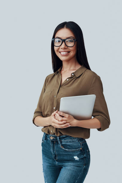istock Confident and smart. Attractive young Asian woman looking at camera and smiling while standing against grey background 1162963691