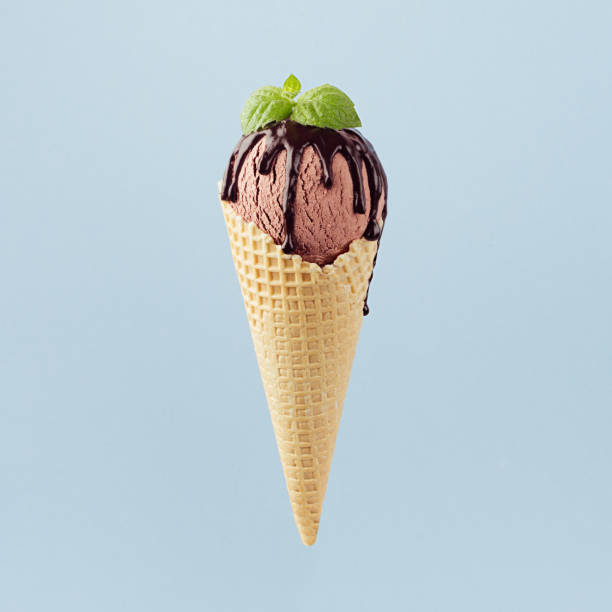 istock Brown creamy ice cream in waffle cone with chocolate sauce, green mint leaf on pastel blue background, square. 1162964365