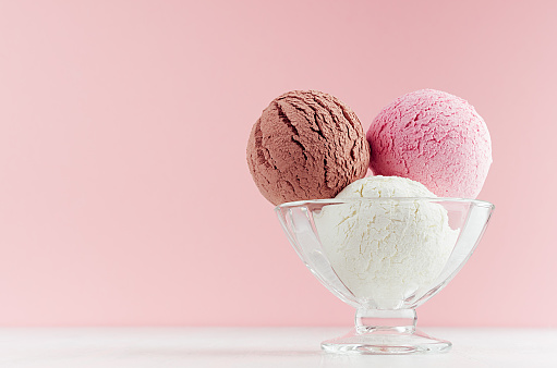 El helado recoge diferentes sabores - fresa, chocolate, cremoso en vaso de helado de vidrio transparente en interior de color rosa moderno en tablero de madera blanca. photo