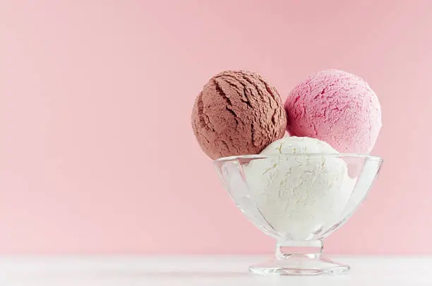 Photo of Ice cream scoops different flavor - strawberry, chocolate, creamy  in transparent glass ice-cream bowl in modern pink color interior on white wood board.