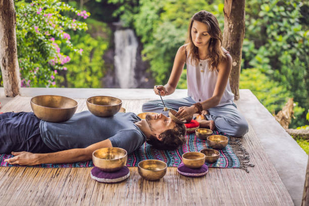 istock Nepal Buddha copper singing bowl at spa salon. Young beautiful man doing massage therapy singing bowls in the Spa against a waterfall. Sound therapy, recreation, meditation, healthy lifestyle and body care concept 1162968752