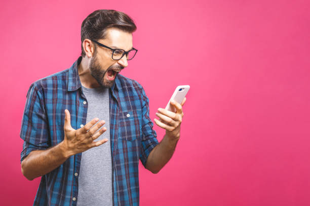 homem caucasiano novo irritado, frustrado e furioso com seu telefone, irritado com serviço de atenção a o cliente sobre o fundo cor-de-rosa. - isolated businessman sadness business person - fotografias e filmes do acervo