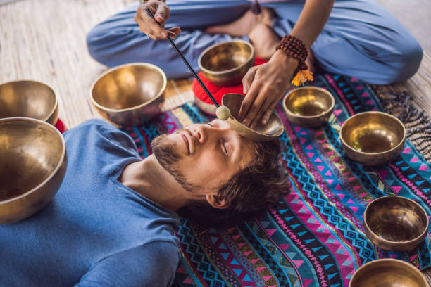 Nepal Buddha copper singing bowl at spa salon. Young beautiful man doing massage therapy singing bowls in the Spa against a waterfall. Sound therapy, recreation, meditation, healthy lifestyle and body care concept. cuenco de canto de cobre nepal buda en el salón de spa. joven hermoso hombre haciendo terapia de masaje cantando cuencos en el spa contra una cascada. terapia de sonido, recreación, meditación, estilo de vida saludable y concepto de cuidado corporal