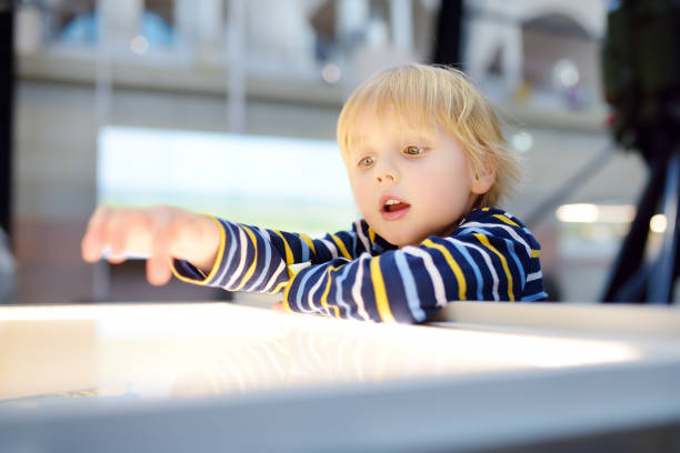 Little aucasian boy is looking at an illuminated info panel. Education and entertainment for children. Activities for family with preschooler kids.