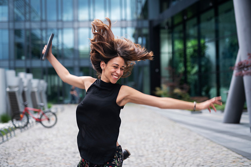 Latino businesswoman jumping around luxury office building exterior outdoor.