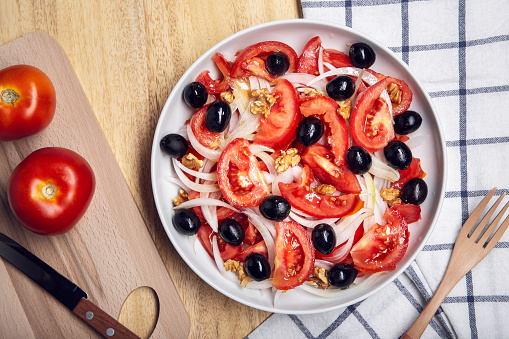 Tasty tomato salad with onion and black olives on plate. Mediterranean food. Top view