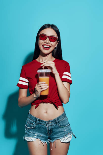 istock Perfect refreshment. Attractive young Asian woman smiling while standing against blue background 1162975093