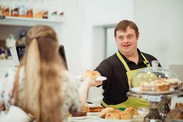A Person With Down Syndrome Serving in a Cafe A man with Down syndrome is serving a scone to a woman in a cafe where he works. waiter photos stock pictures, royalty-free photos & images