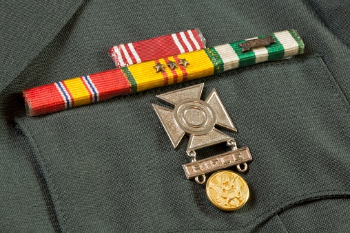 Close up view of the metals on a US Army dress jacket from the Vietnam era.  The gold or brass US eagle buttons stand out against the green uniform.  Medals include the National Defense Ribbon, Republic of Vietnam (RVN) Campaign Ribbon, Vietnam Service Ribbon with bronze stars, Good Conduct Ribbon and Rifle Sharpshooter medal.