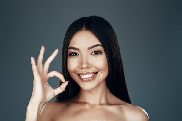 istock Everything is OK. Beautiful young Asian woman looking at camera and smiling while standing against grey background 1162980265