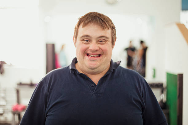 A close-up portrait of a person with Down syndrome standing indoors and smiling towards the camera.