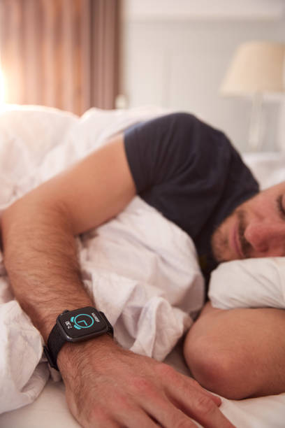 istock Man Asleep In Bed Wearing Smart Watch As Sun Breaks Through Curtains 1162987177
