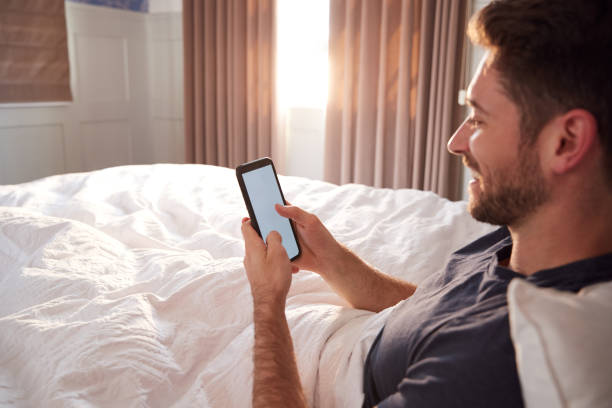 istock Man Sitting Up In Bed Looking At Mobile Phone After Having Woken Up 1162987427