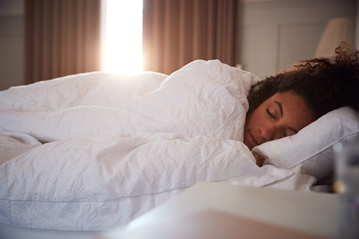 Mujer pacífica durmiendo en la cama mientras el día rompe las cortinas photo