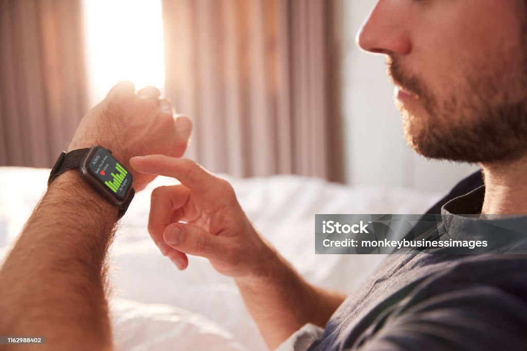 Man Sitting Up In Bed Looking At Screen Of Smart Watch Smart Watch Stock Photo