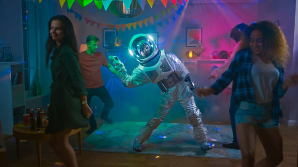 At the College House Costume Party: Fun Guy Wearing Space Suit Dances Off, Doing Robot Dance Modern Moves. With Him Beautiful Girls and Boys Dancing in Neon Lights. At the College House Costume Party: Fun Guy Wearing Space Suit Dances Off, Doing Robot Dance Modern Moves. With Him Beautiful Girls and Boys Dancing in Neon Lights. cosmonaut photos stock pictures, royalty-free photos & images