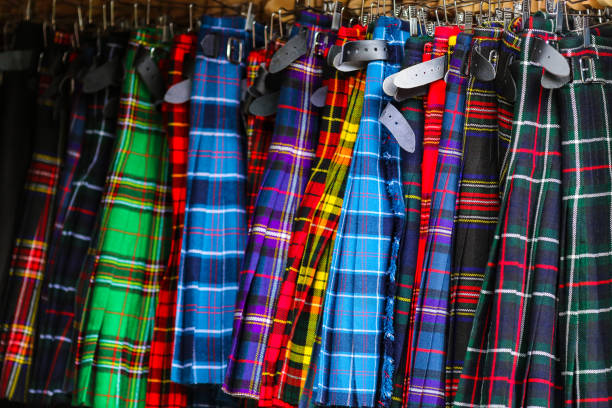 A collection of colorful men's plaid kilts with belts on display for sale in a store