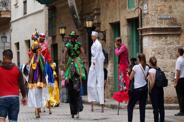 Colorful street performers in La Habana vieja area. Group of artist wearing bright colorful costumes and walking around in tall stilts. A bunch of tourist taking pictures of the performance. Taken on a clouded afternoon.