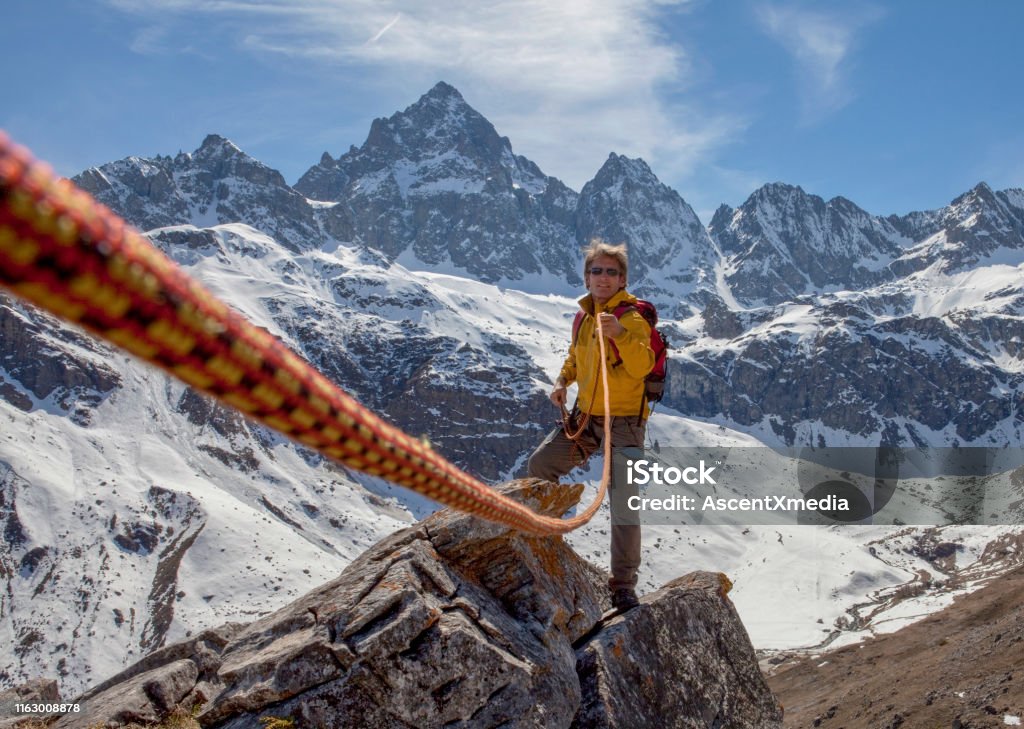 Climbing rope leads to mountain guide on rock summit Snowcapped mountains in the distance Guide - Occupation Stock Photo