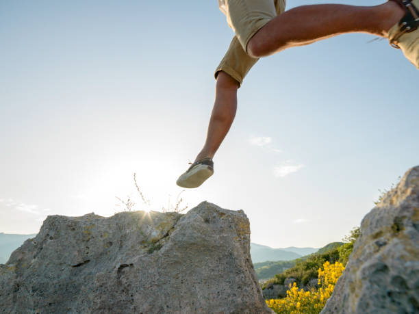 Hiker jumps onto rock at sunrise Hills in distance leap of faith stock pictures, royalty-free photos & images