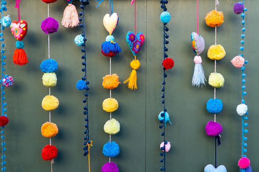 Several colorful pom pom garlands hang vertically against a green wall in Olivera Street Los Angeles