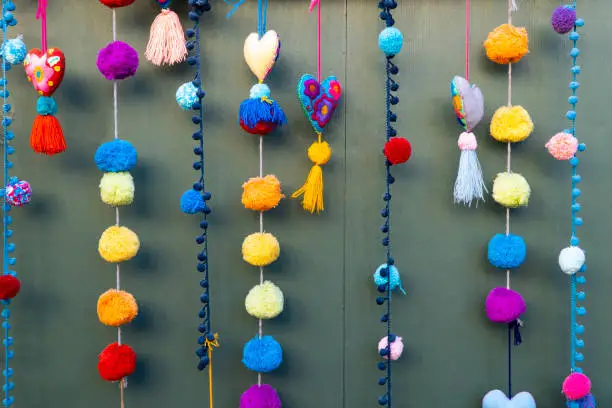 Several colorful pom pom garlands hang vertically against a green wall in Olivera Street Los Angeles