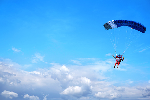 Skydiver with a blue canopy of a parachute on the background a blue sky and clouds, close-up. Skydiver under parachute above the stormy clouds