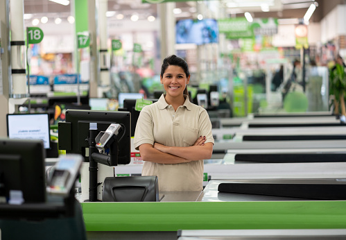 Beautiful cashier at a supermarket smiling at camera with arms crossed very confident - Business industry concepts