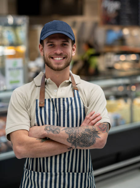 schöne betreuer einer feinkostabteilung, die auf die kamera schaut und lächelnd mit gekreuzten armen lächelt - supermarket meat store manager stock-fotos und bilder