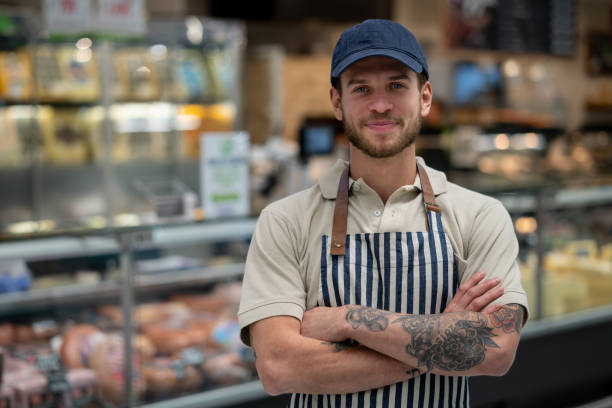 friendly manager of a delicatessen with arms crossed facing camera smiling - supermarket meat store manager imagens e fotografias de stock