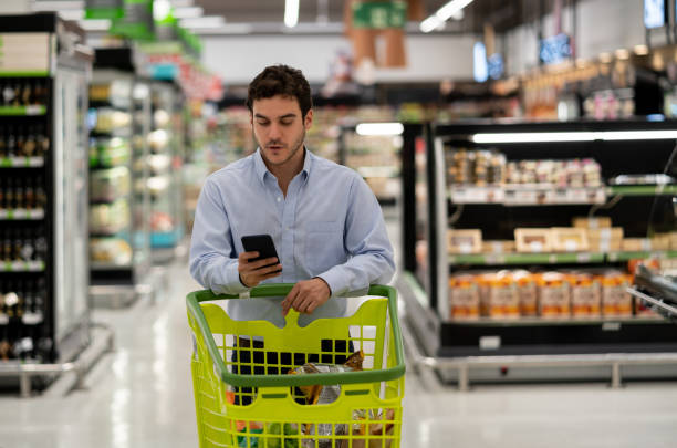 istock Single guy at the supermarket using a mobile app for shopping list while pushing cart 1163012828