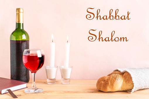 Shabbat or Shabath concept. Challah bread, shabbat wine, book and candles on table, copy space. Traditional Jewish Shabbat ritual.