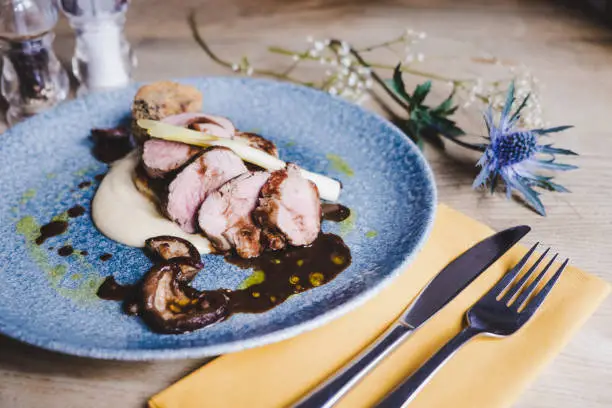 Plate of pork fillet served in a restuarant, ararnged with yellow and blue tones and flower detail
