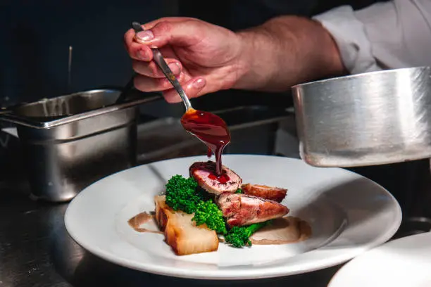 Close up shot of gravy being poured onto a main course in a commercial kitchen environment