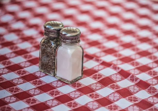 salt and pepper shakers sitting on a red and white checkered table cloth at an outside restaurant.
